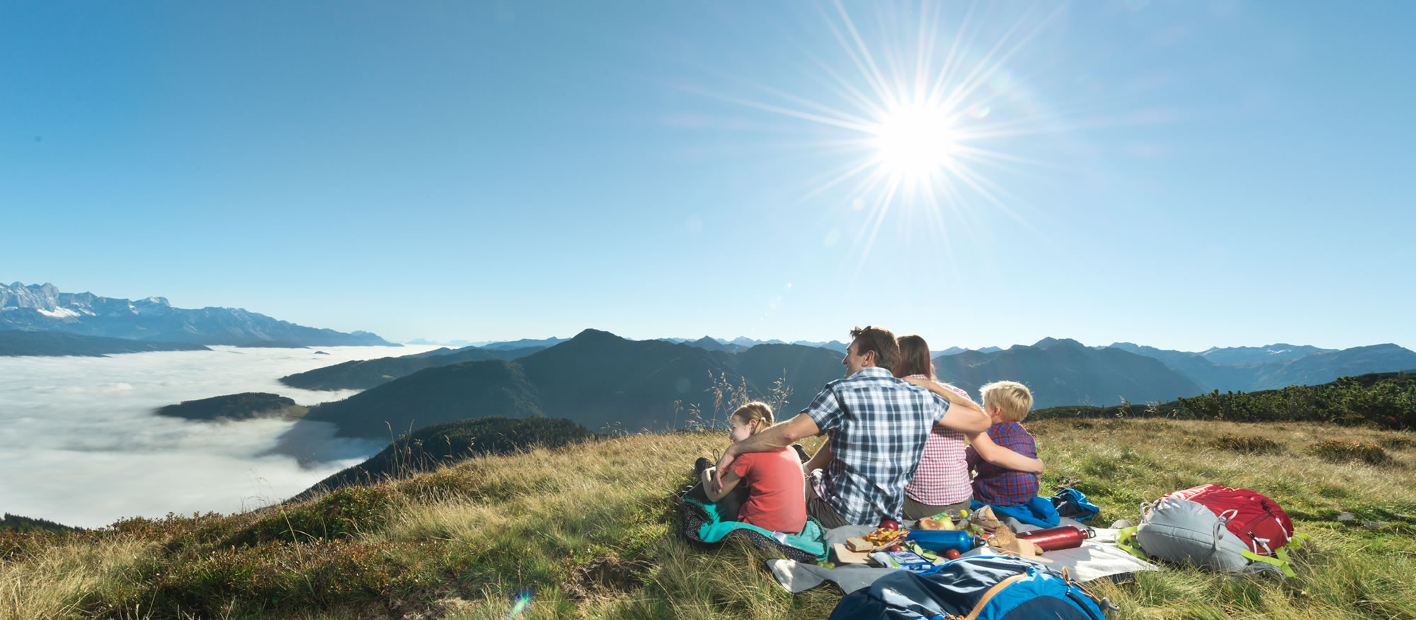 Familie blickt bei Sonnenschein auf Bergpanorama © Flachau Tourismus
